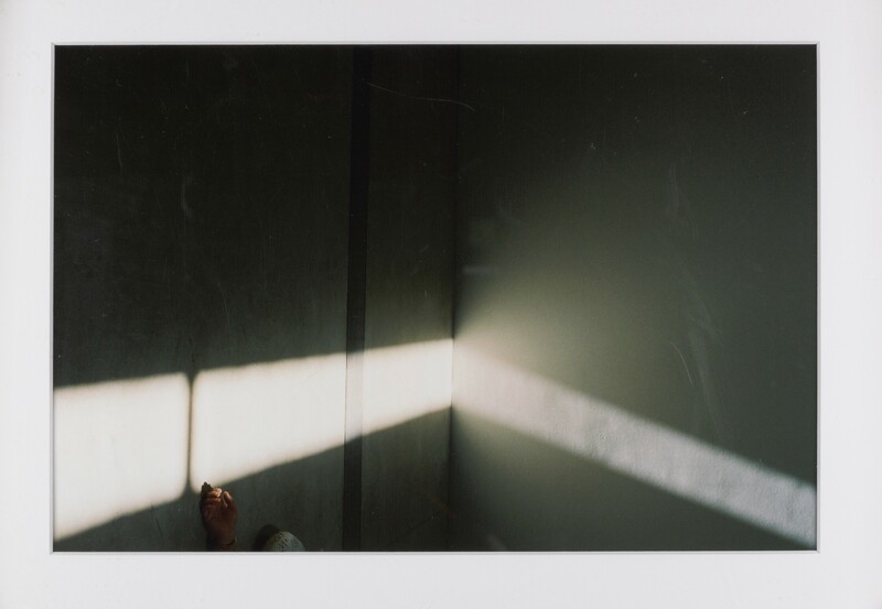 Framed photograph of a hand reaching into a beam of light. The shadows are dark at the top, gradually becoming lighter. 